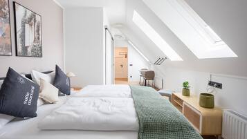 Een moderne slaapkamer met dakraam, een bed met witte lakens, een groene plaid en een kleine plant op een nachtkastje.