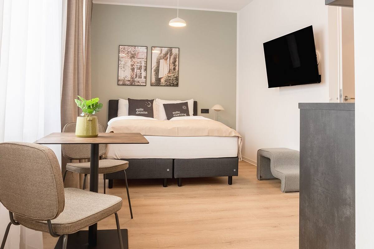 Quarto de hotel moderno com cama, escrivaninha, cadeira, televisão e obras de arte na parede.