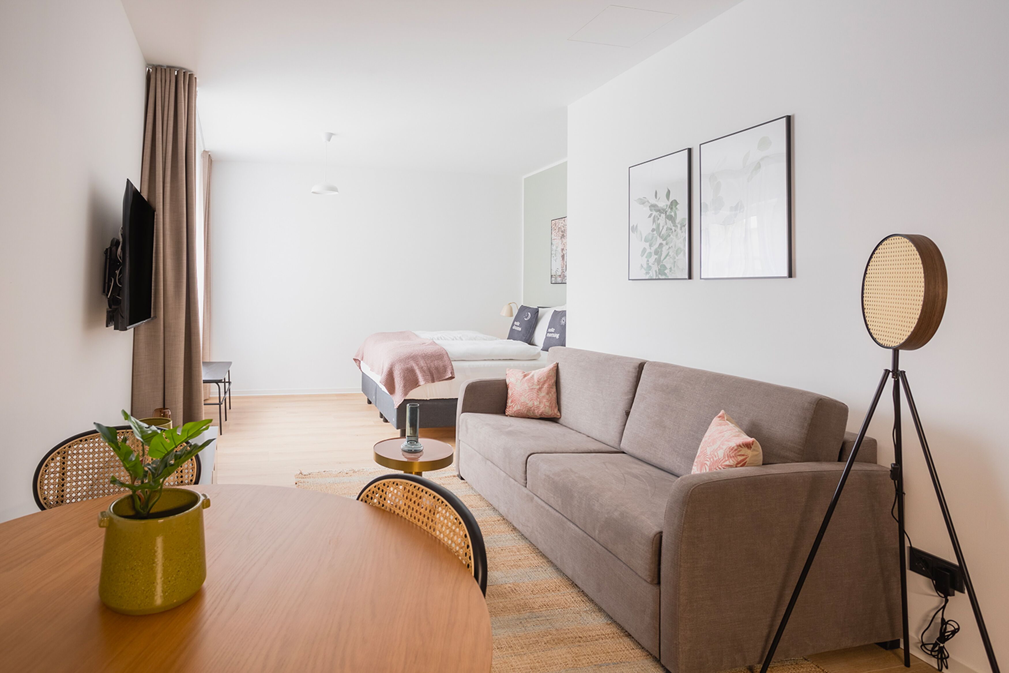 Une chambre d’hôtel moderne avec un canapé, une table à manger, un téléviseur fixé au mur et un lit en arrière-plan.