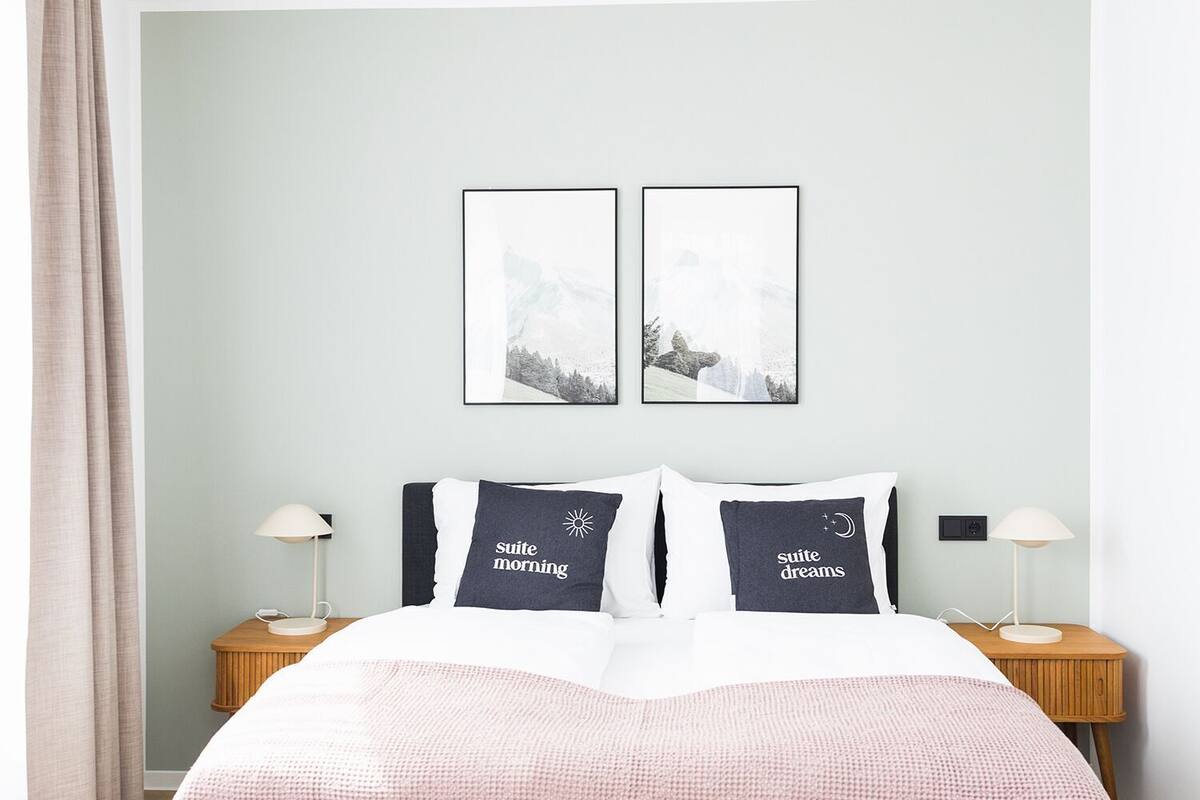 Um quarto moderno com uma cama, duas mesas de cabeceira, um criado-mudo e obras de arte na parede.