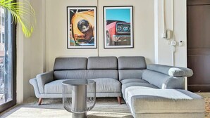 A modern living room with a grey sectional sofa, a small round table, and two framed pictures on the wall. - w* | Premium 1BR in Casco Antiguo (Panamá)