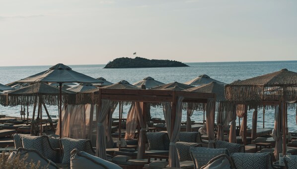 Un espace de détente aménagé sur la plage, avec des parasols en chaume et des chaises longues, offrant une vue sur la mer.