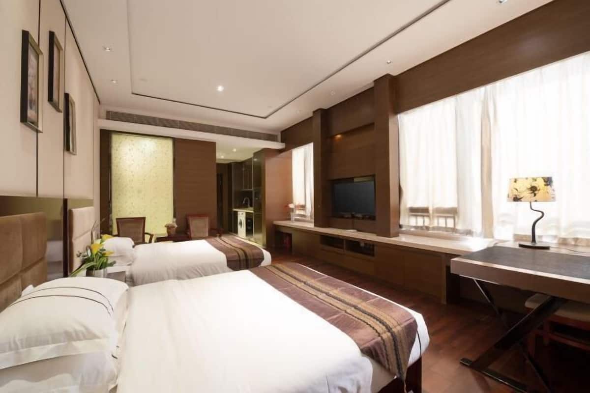 A hotel room with two beds, a desk, a television, and a window with curtains.