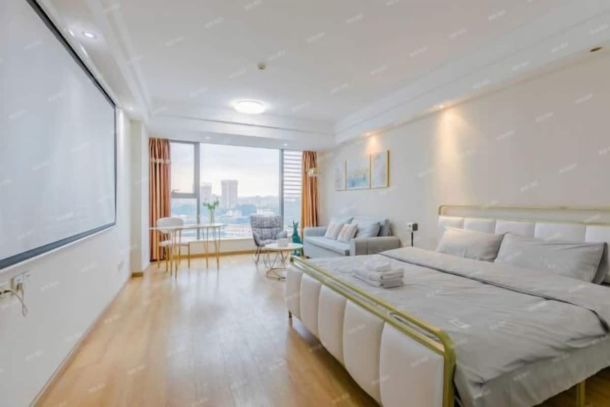 A modern hotel room with a large bed, a desk, and a view of the city.