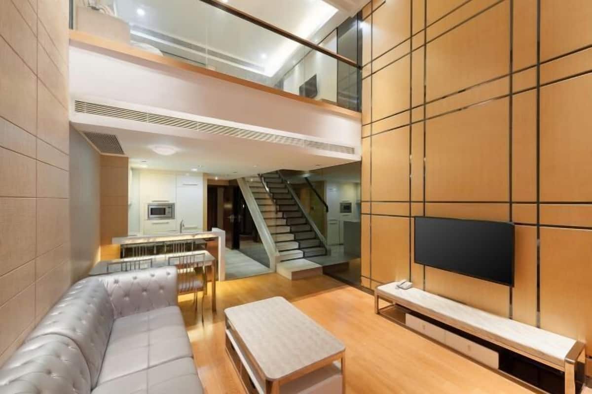 A modern interior with a sofa, a coffee table, a TV mounted on a wall, and a staircase leading to an upper level.