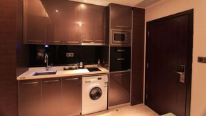 A compact kitchen with a washing machine, microwave, and dark wooden cabinets.