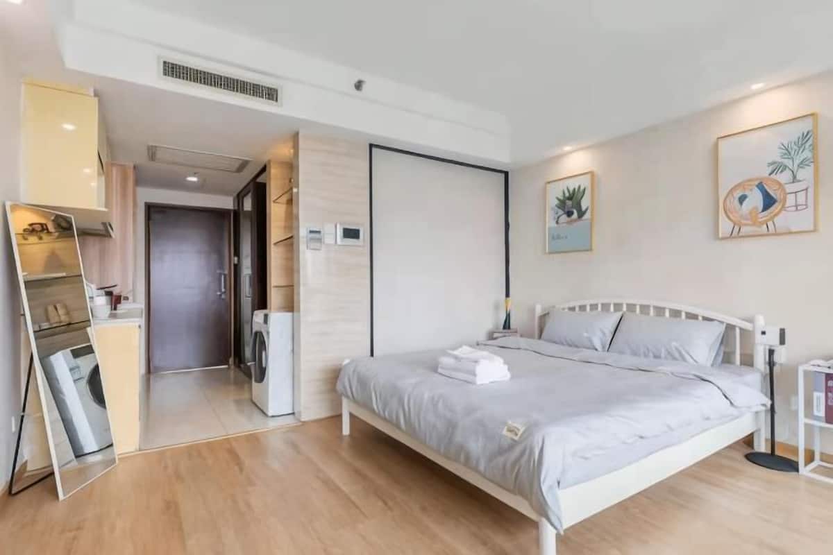 A modern hotel room with a bed, a wardrobe, a mirror, and a door leading to a bathroom.