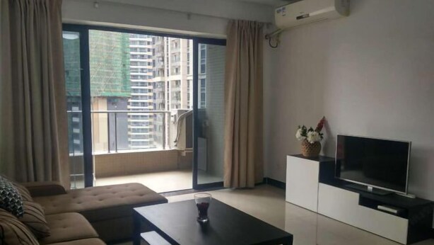 A modern living room with a sofa, a coffee table, a TV on a cabinet, and a balcony with curtains.