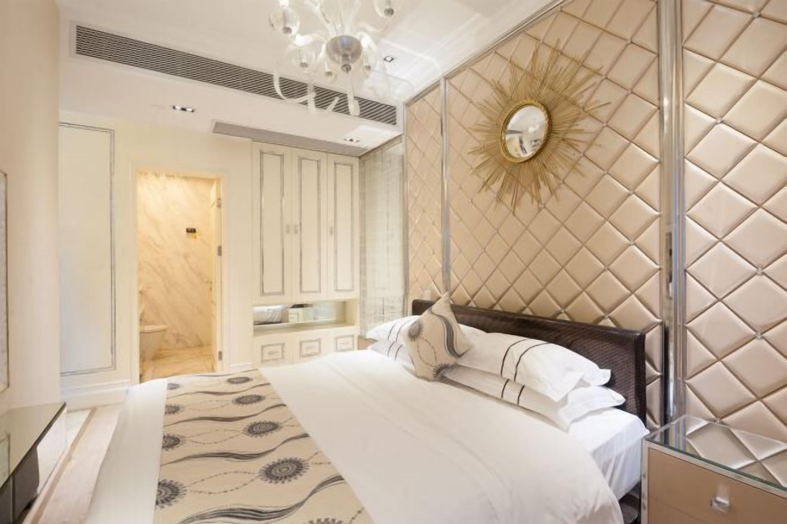 A bedroom with a large bed, a vanity with a mirror, and a wall-mounted sunburst light fixture.