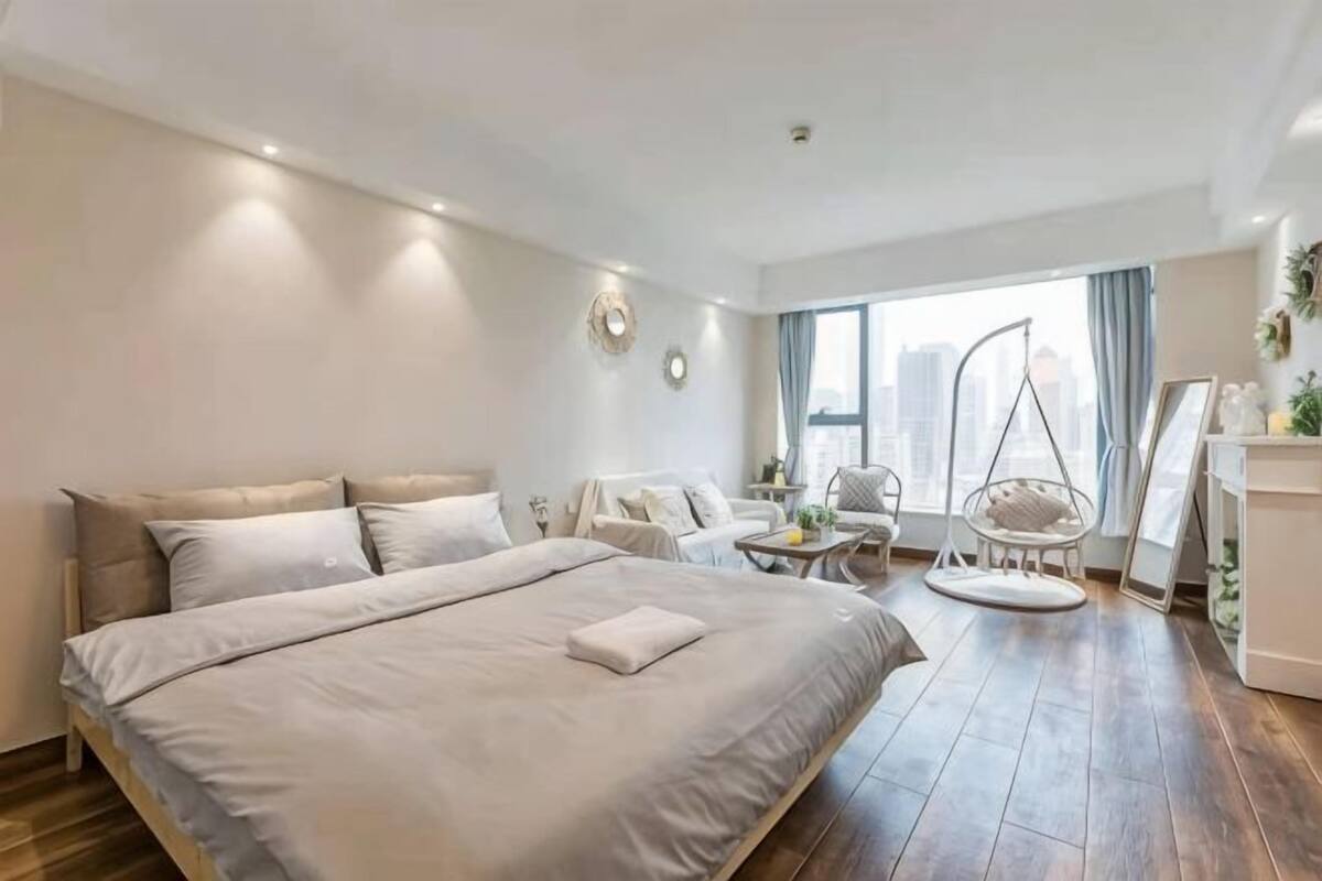 A modern hotel room with a large bed, a sitting area with chairs, a small table, and a view of the city.