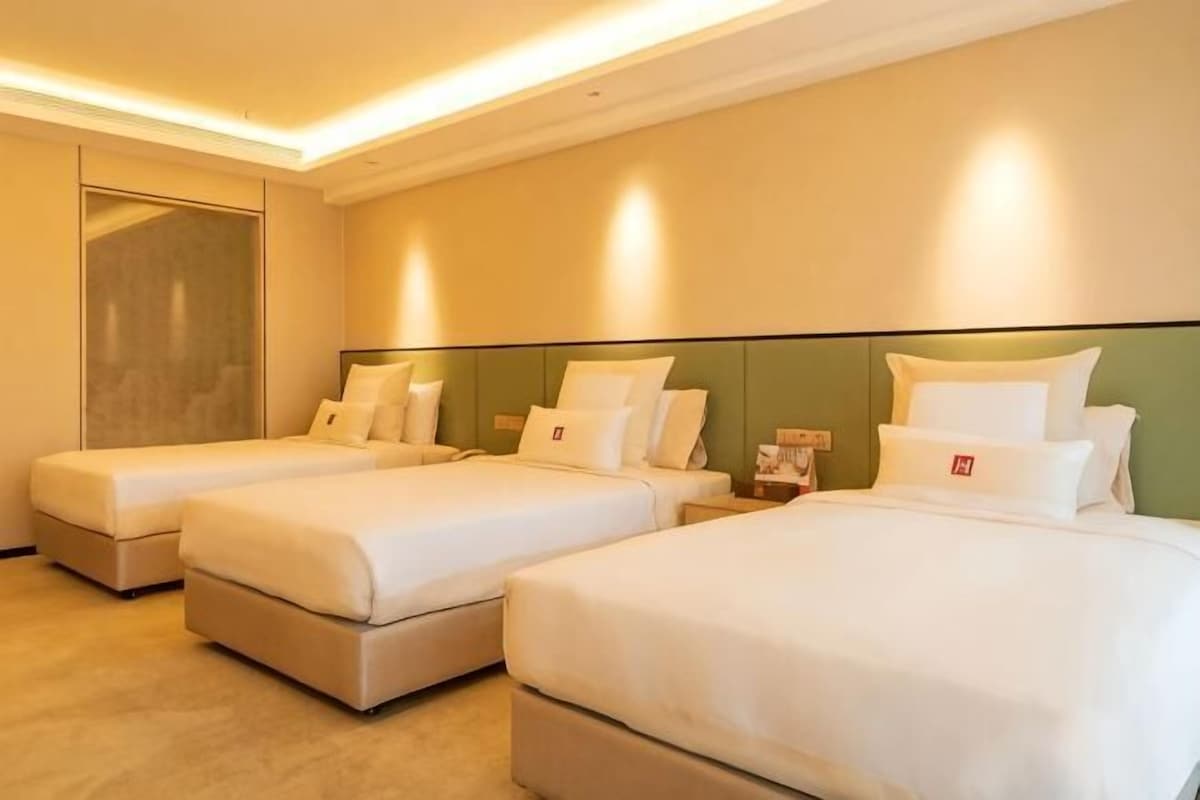 Una habitación de hotel con tres camas, un espejo grande y un cabecero verde.
