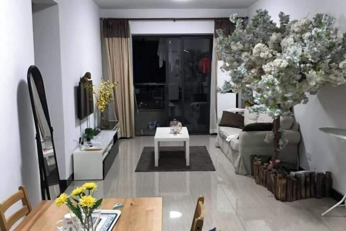 A modern living room with a dining area, a sofa, a coffee table, and a decorative tree.