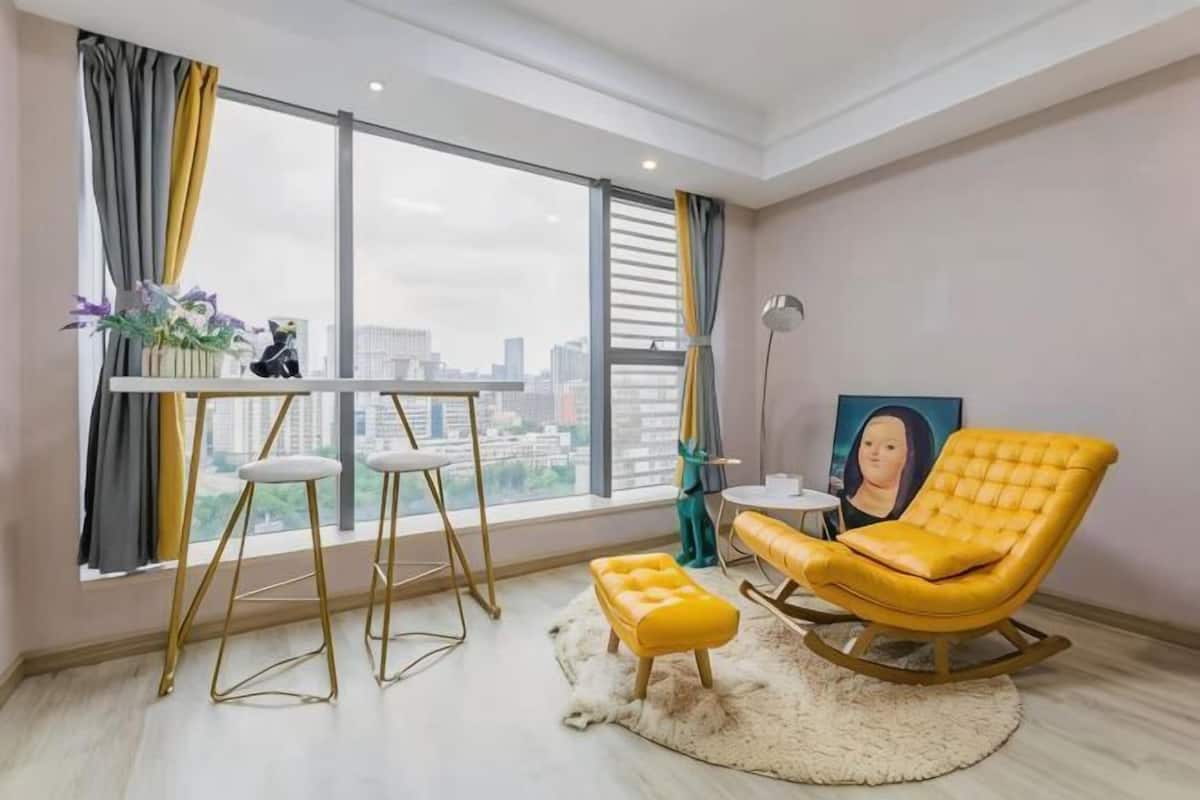 A room with a city view, a yellow chair, a small table, and a white ottoman.