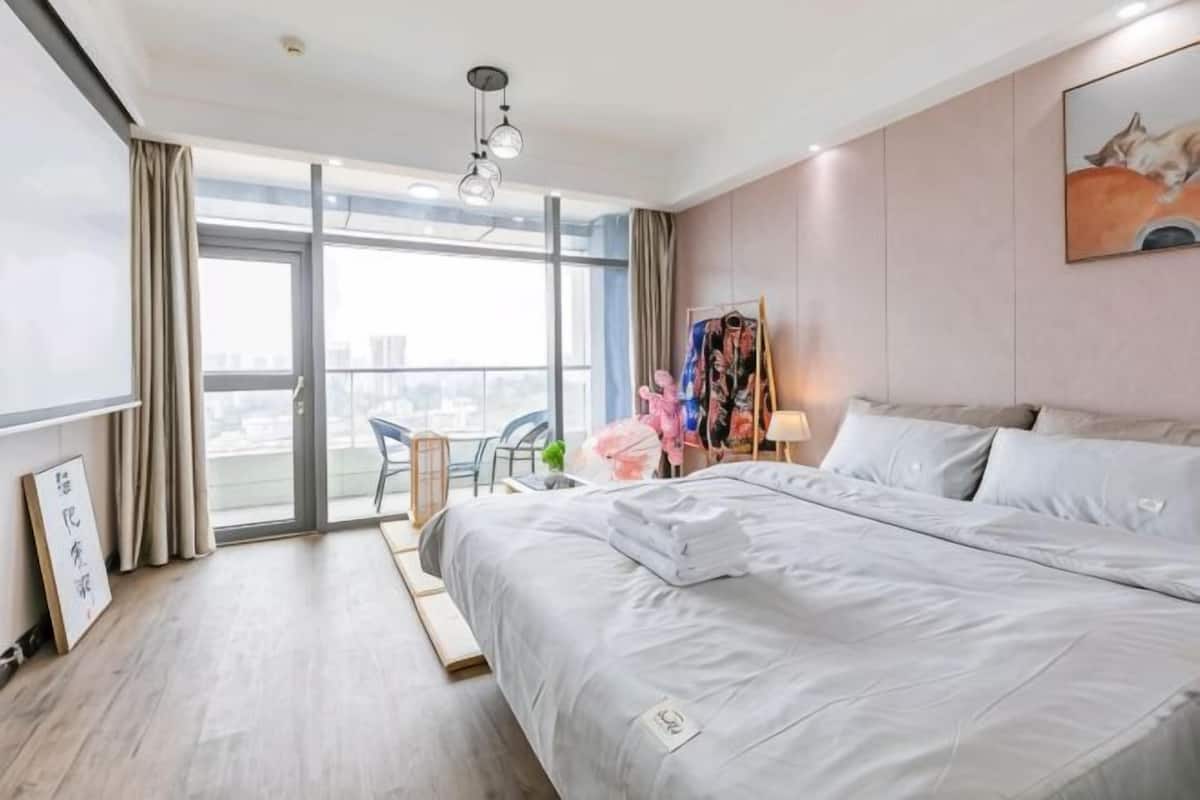 A hotel room with a large bed, a desk, a chair, and a view of the city through the window.