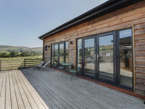 A wooden cabin with a deck, large sliding glass doors, and a view of the countryside. - Tin Shed (Rhayader)