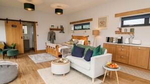 A modern, well-lit living room with a sofa, coffee table, and a dining area with a small table and chairs. - Tin Shed (Rhayader)
