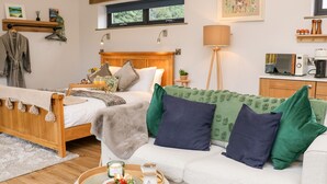 A cozy bedroom with a wooden bed, a bedside table with a lamp, a green sofa, and a breakfast tray with pastries and coffee. - Tin Shed (Rhayader)