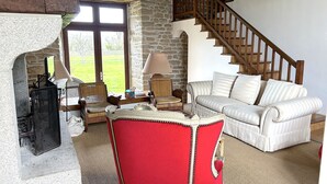 A cozy living room with a stone wall, a fireplace, a staircase, and a white sofa.