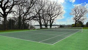 A tennis court with a net, surrounded by trees and a fence.