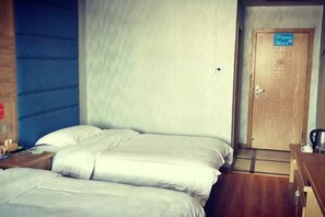 Habitación de hotel con dos camas, una puerta de madera y una mesita con hervidor.