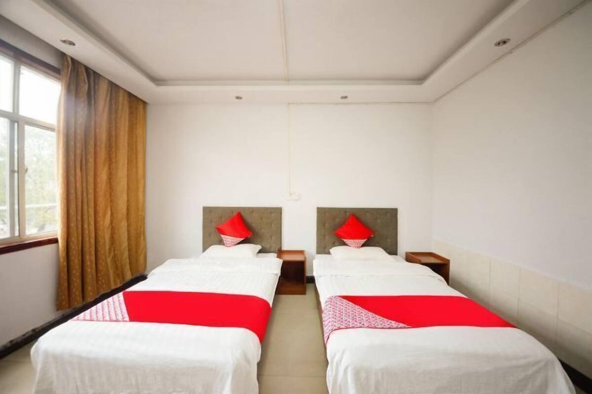 A hotel room with two beds, a window with curtains, and a plain white wall.