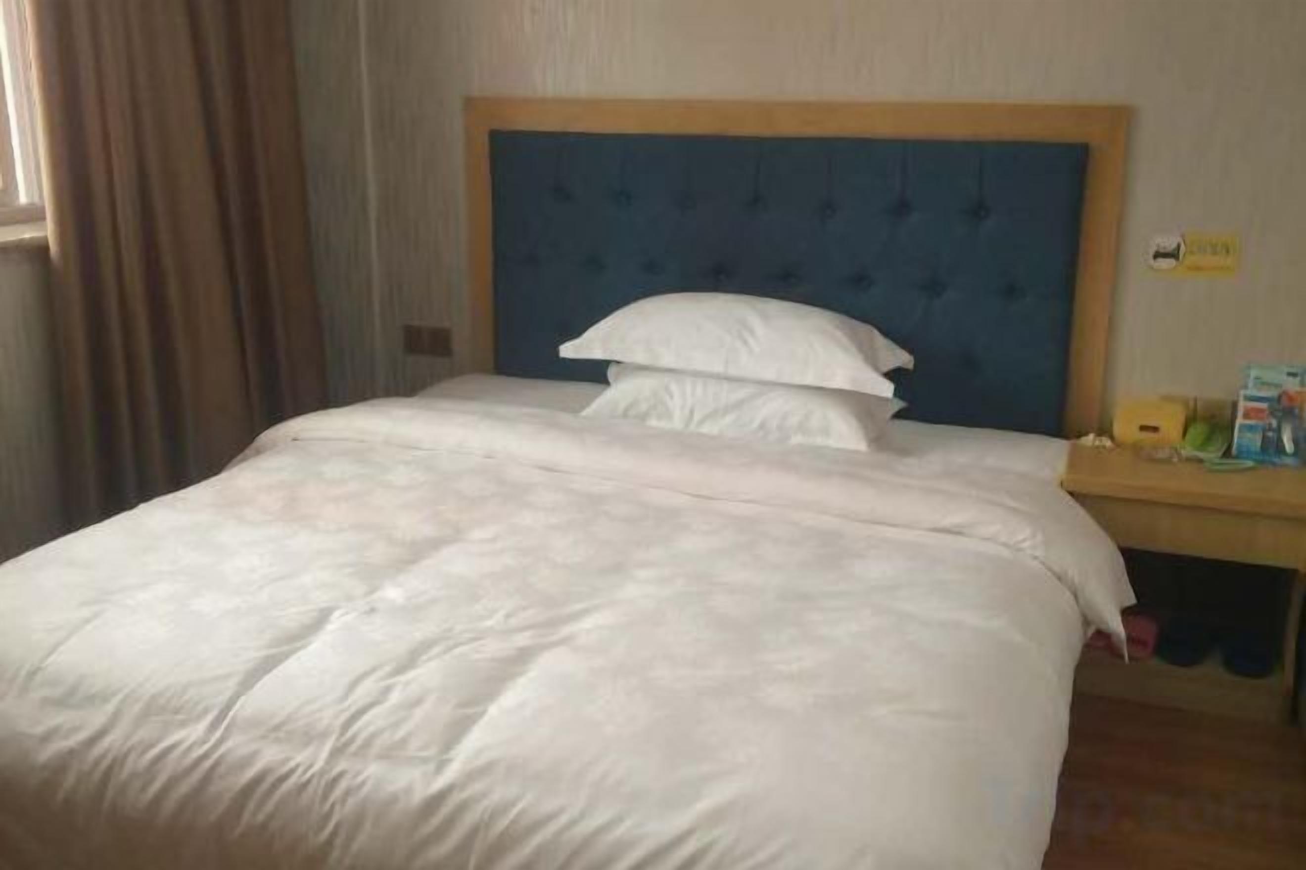 A hotel room with a large bed, a wooden headboard, a bedside table with a lamp, and a window with curtains.