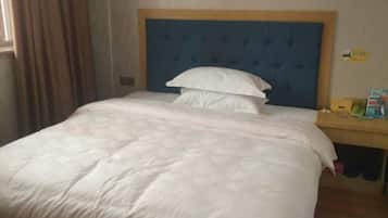 A hotel room with a large bed, a wooden headboard, a bedside table with a lamp, and a window with curtains.