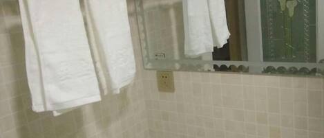 A bathroom with white towels hanging on a rack, a mirror above the sink, and a window with a view of flowers.