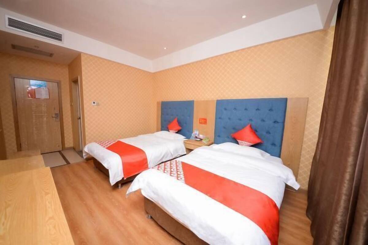 A hotel room with two beds, a wooden floor, a blue headboard, and a door with a mirror.