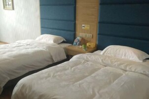 A hotel room with two beds, a wooden headboard, and a small table with a lamp and some items on it.