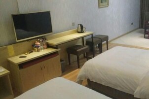 Habitación de hotel con cama, escritorio, silla, televisión y una pequeña mesa con cafetera.