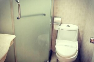 Baño con cabina de ducha de vidrio, inodoro y dispensador de toallas de papel.