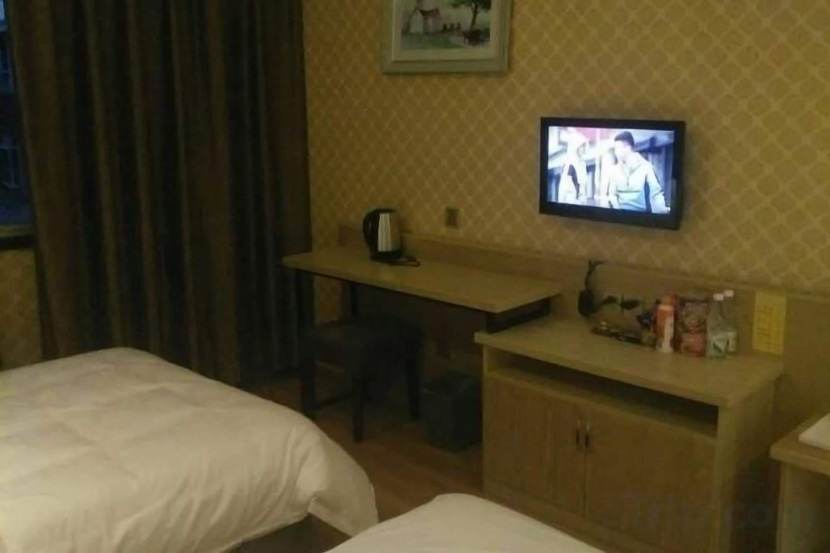 A hotel room with two beds, a desk, a television, and a small kitchenette.