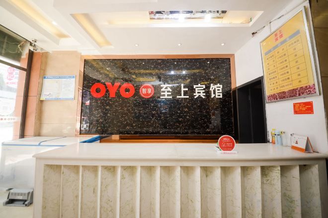 A reception desk with a black marble top and a white counter. There is a red circular sign on the counter, and a wall with a bulletin board to the right.