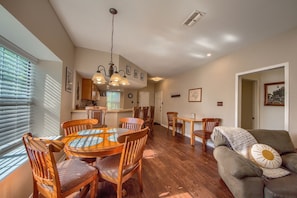 A dining area with a round wooden table and chairs, a chandelier, and a cozy living room with a sofa and a throw blanket.