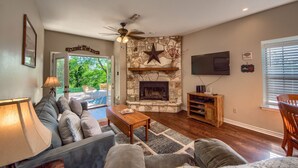A living room with a stone fireplace, a ceiling fan, and a television mounted on the wall.