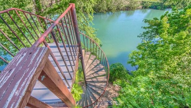 A spiral staircase leading to a platform overlooking a calm river surrounded by lush greenery.