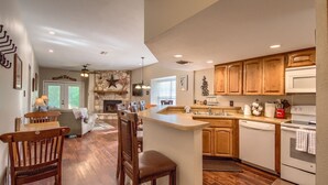 A kitchen with wooden cabinets, a central island, a stone fireplace, and a dining area with chairs and a sofa.