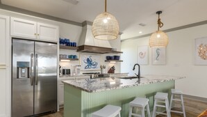 A modern kitchen with a stainless steel refrigerator, a marble island with bar stools, and decorative wall art.