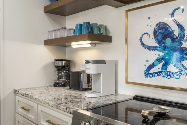 A kitchen with a coffee maker, toaster, and a shelf with cups.