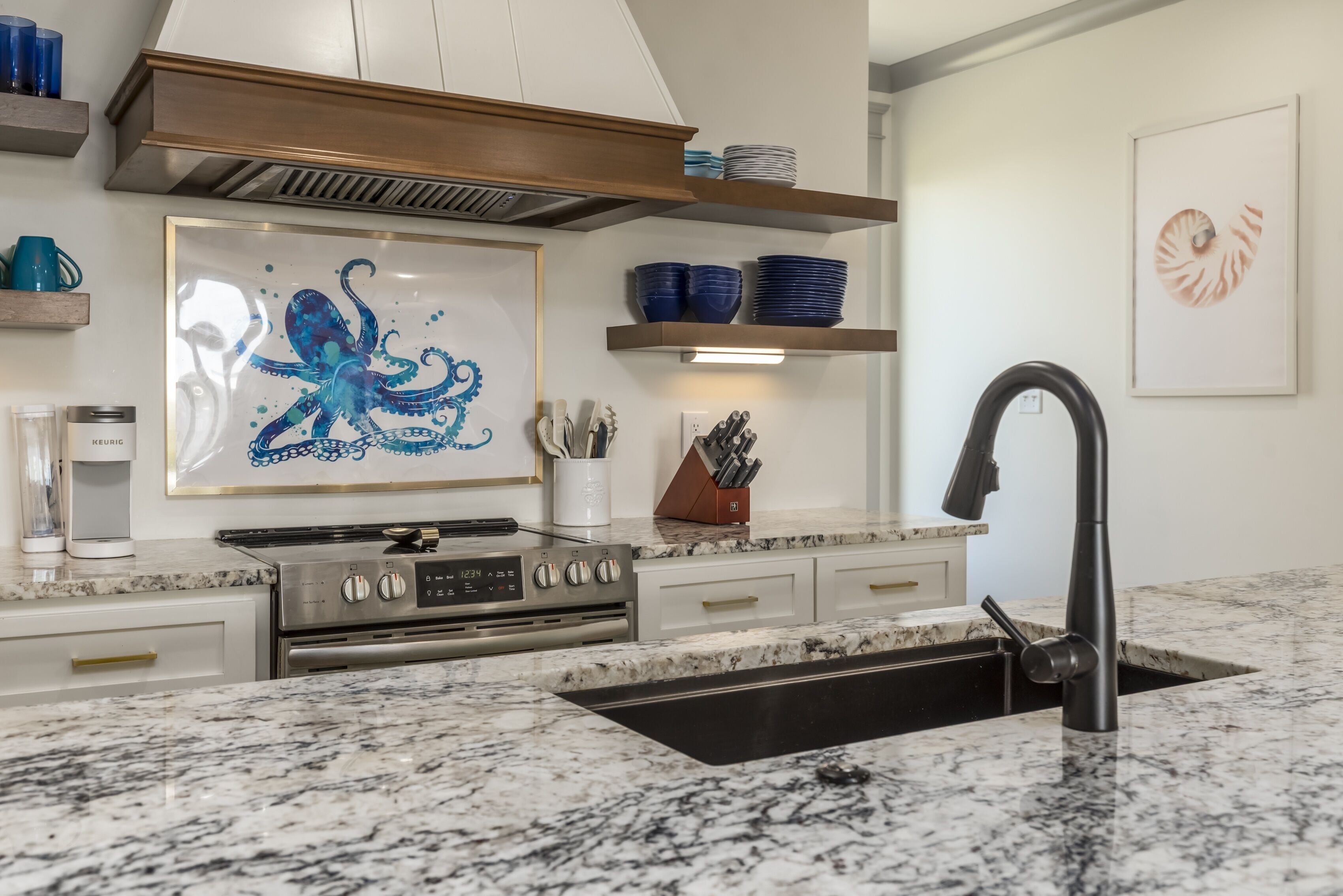 Una cocina moderna con estufa de acero inoxidable, un lavamanos negro y encimera de mármol.