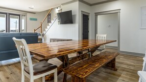 A dining area with a large wooden table, white chairs, and a bench.
