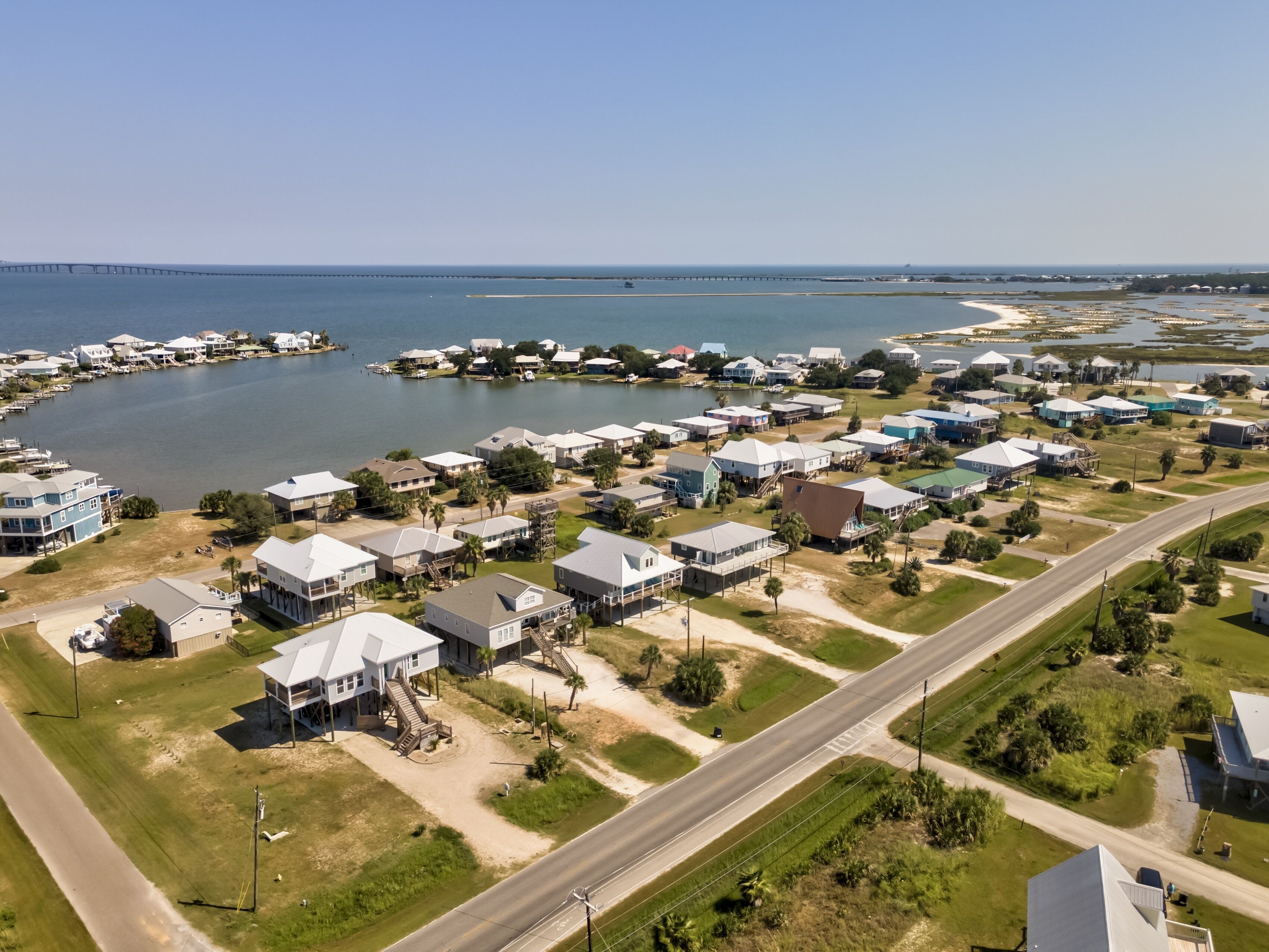 An aerial view of a coastal residential area with houses, a marina, and a bridge.