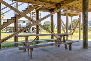 A wooden picnic table under a wooden structure with a view of houses in the background.