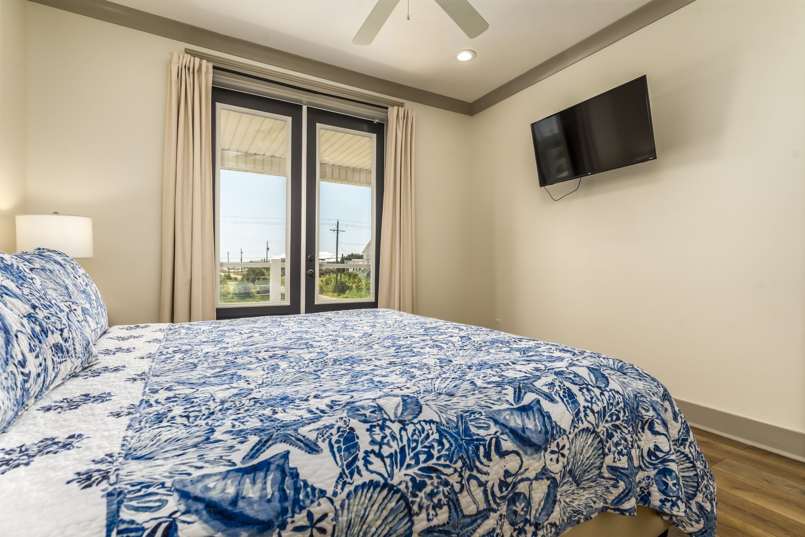 Ein Schlafzimmer mit einem großen Bett, einem an der Wand befestigten Fernseher und einem Fenster mit Vorhängen.