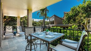 Un patio exterior con una mesa lista para comer, rodeada de sillas y vistas a un edificio y follaje.