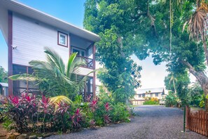 A two-story building with a balcony, surrounded by lush greenery and a gravel driveway. - Casa Palmera 2 Bedroom Home by RedAwning (Roatan)