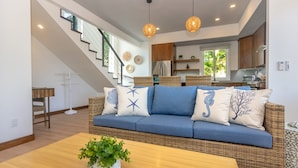 A modern living room with a blue sofa, wicker furniture, and a staircase leading to an upper level. - Casa Palmera 2 Bedroom Home by RedAwning (Roatan)