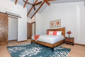 A bedroom with a wooden bed, a nightstand, a vase with flowers, and a ceiling fan. - Casa Palmera 2 Bedroom Home by RedAwning (Roatan)