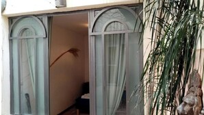A room with a sliding glass door leading to a balcony, a potted plant, and a small table with a bowl. - Aigues-Mortaise house in the city (Aigues-Mortes)